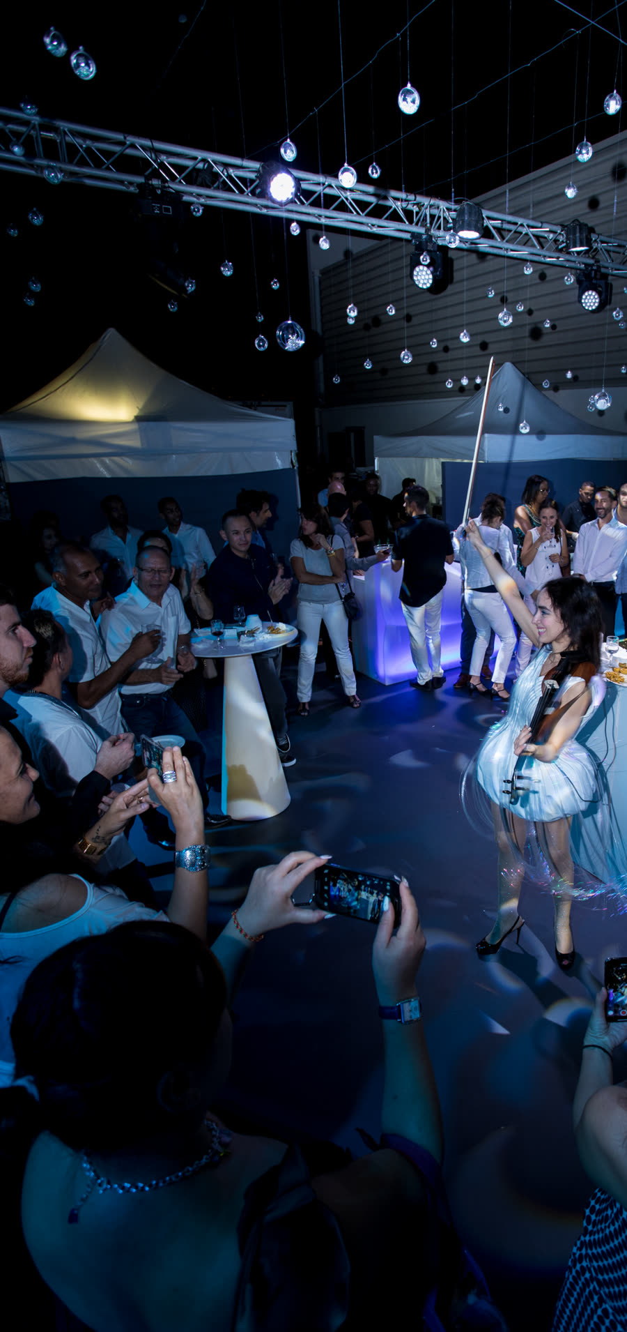 Sadie in the light dress playing amid a crowd at a brand evening, phones raised