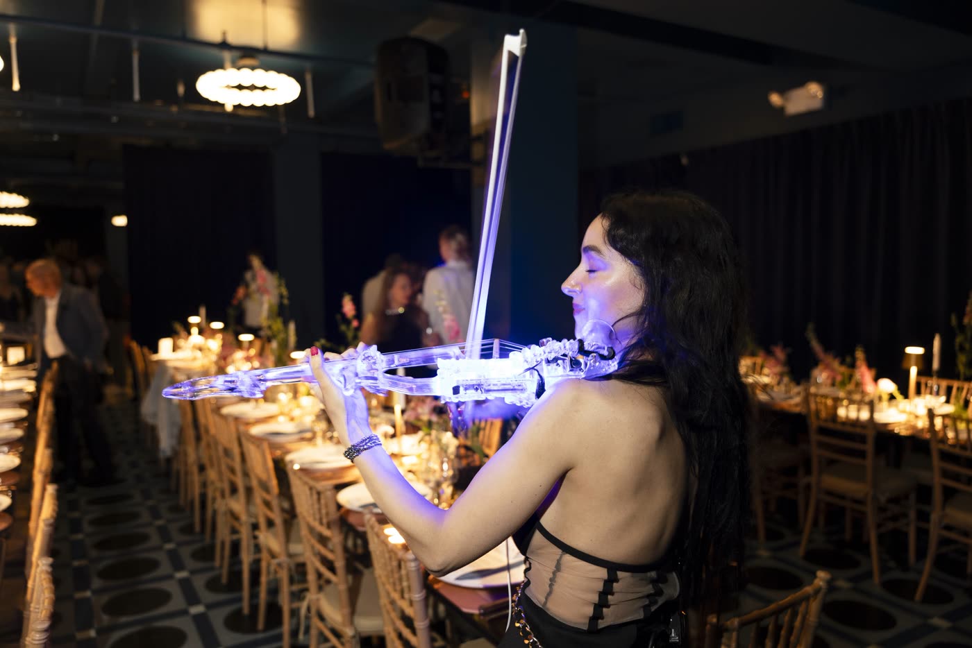Sadie playing the transparent violin, glowing blue over a candlelit dinner room