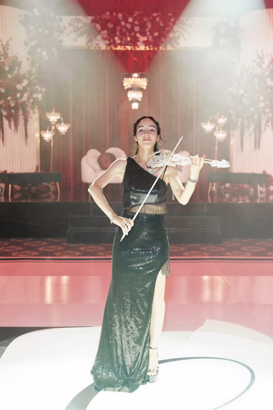 Sadie playing the transparent violin on a haze-lit dance floor, chandeliers behind her