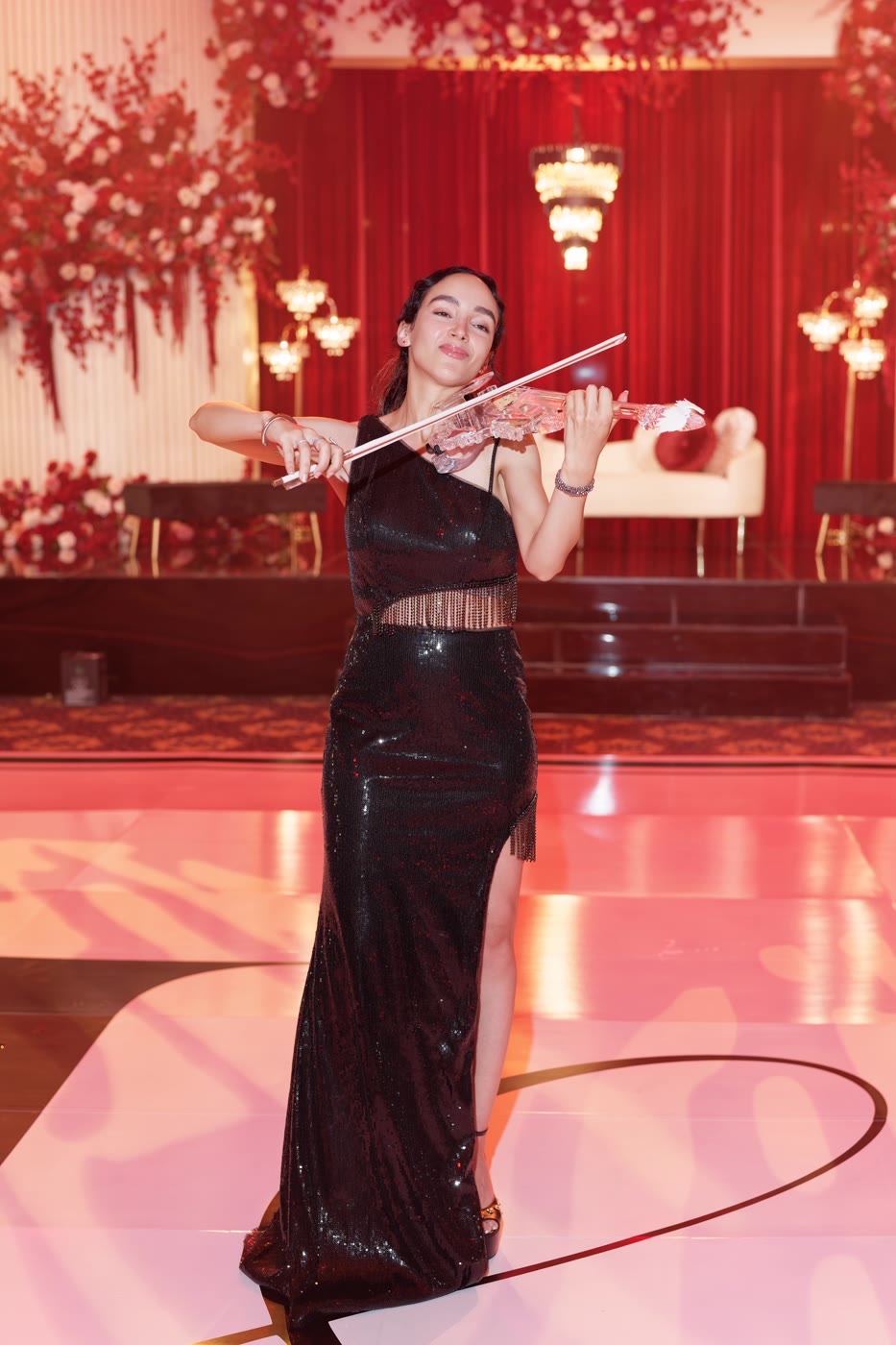 Sadie playing the transparent violin on a red ballroom stage at a black-tie evening