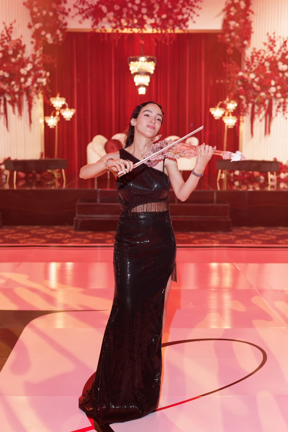 Sadie Varius playing the transparent violin at a black-tie evening, red-lit stage behind her